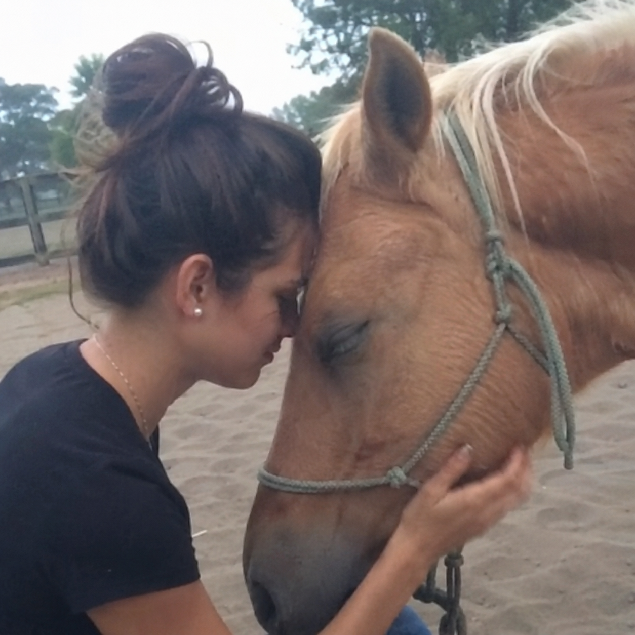 A woman resting her forehead against a palomino horse in a quiet moment of connection